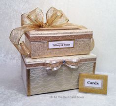 two boxes are stacked on top of each other with gold ribbons and tags attached to them