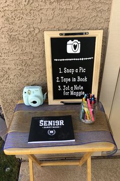 a small table with a sign on it and some pens, pencils, and a camera