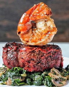 a piece of steak with shrimp on top of it and spinach in the foreground