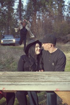 a man and woman sitting at a picnic table with an old truck in the background