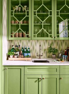 a kitchen with green cabinetry and white counter tops, filled with bottles and glasses