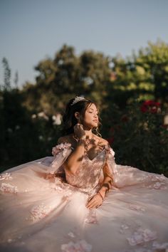 a woman sitting on the ground wearing a dress and tiara with flowers in her hair