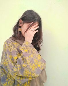 a woman with her hand on her face and wearing a scarf over her head, standing against a wall