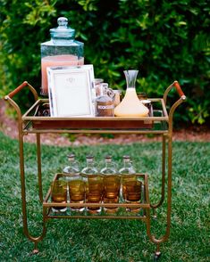 an old fashioned bar cart with liquor bottles on it in the grass next to bushes