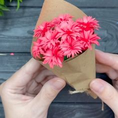 someone holding a bouquet of pink flowers in their hand on a wooden table with other flowers