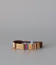 a brown leather bracelet with gold beads and tassels on the end, sitting against a gray background