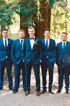 a group of men standing next to each other wearing suits and ties in front of trees