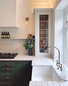 a kitchen with green cabinets and white counter tops, wine glasses on the cabinet doors