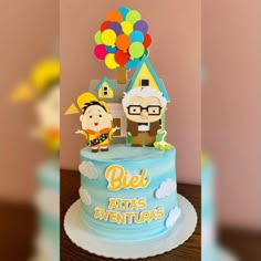 a blue cake with two people on top and balloons in the air above it that says biel atlas aventuras