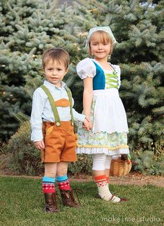 two young children standing next to each other in front of some bushes and trees with one holding the hand of another child's hand