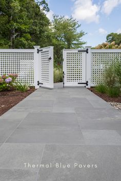 two white gates are open on the side of a walkway in front of a garden