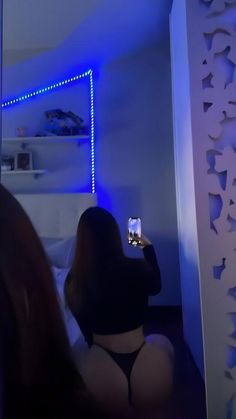 a woman taking a selfie with her cell phone in front of a mirror that has blue lights on it