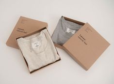 two shirts in a box on a white surface with a brown cardboard box behind them