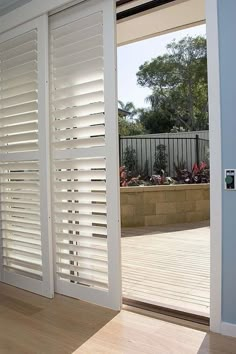 an open door with white shutters and wood flooring in front of a patio