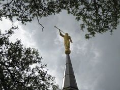 a statue on top of a tall building with trees in the foreground and clouds in the background