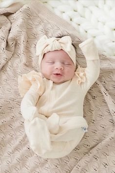 a baby laying on top of a bed wearing a white hat and sweater with a bow