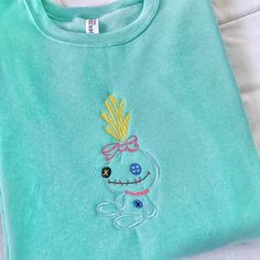 a blue shirt with a cartoon character on it's chest and an embroidered pineapple on the back