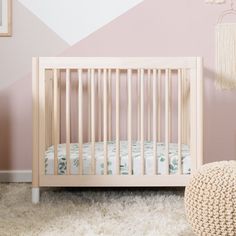 a baby crib in front of a pink wall with white and green decor on it