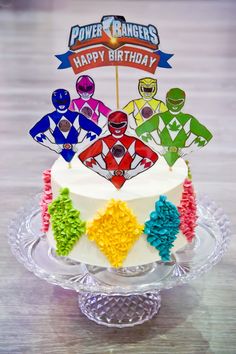 a birthday cake decorated with the power rangers on top of a glass platter that says happy birthday