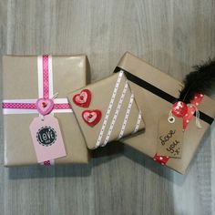 three wrapped gift boxes with tags and hearts on them sitting on a wooden floor next to each other