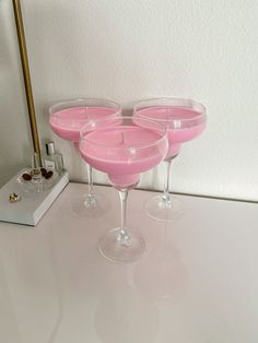 three wine glasses sitting on top of a white counter next to a gold candle holder