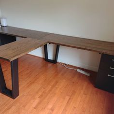 a wooden desk sitting on top of a hard wood floor next to a white wall