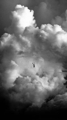 black and white photograph of a person in the sky with clouds behind them, flying through the air