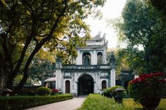 an old building surrounded by lush green trees and flowers in the foreground is a walkway leading to it