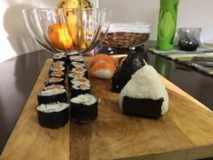 some sushi on a wooden board near a bowl of fruit