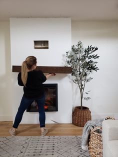 a woman standing in front of a fireplace with a potted plant next to it