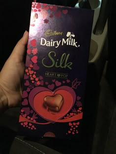 someone holding up a box of dairy milk with a heart on the front and side