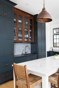 a kitchen with dark blue cabinets and white countertops is pictured in this image, there are two wooden chairs at the center of the table