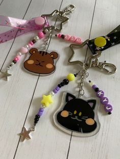 several keychains with different designs and colors on white wooden floor, including a black cat