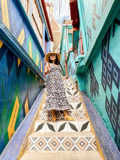 a woman in a hat is walking up some stairs with colorful painted walls and steps