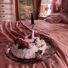 a strawberry cake on a glass plate with a knife sticking out of it, sitting on a bed