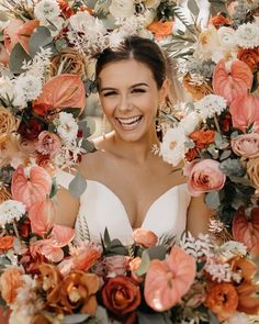 a woman in a wedding dress surrounded by flowers and greenery smiling at the camera