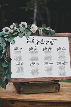 a sign with flowers and greenery on it that says find your seat at the table