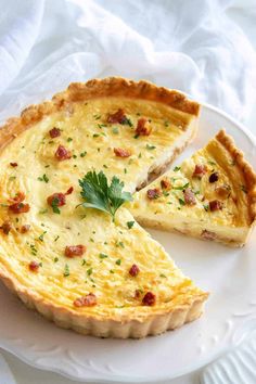 a quiche on a white plate with one slice cut out and garnished with parsley