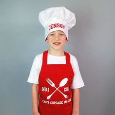 a young boy wearing an apron and chef's hat while standing in front of a gray background