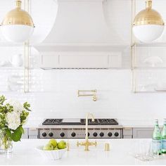 a kitchen with white counter tops and gold accents on the hood, two lights over the stove