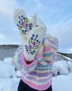 a woman standing in the snow with her hands on her face and wearing mittens