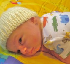 a baby wearing a white hat laying on top of a bed next to a yellow blanket