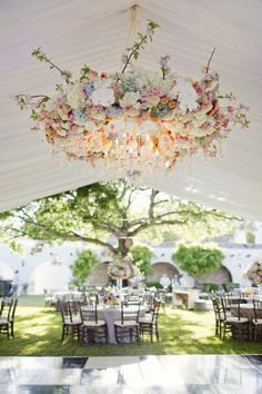 a chandelier hanging from the ceiling in a tent with tables and chairs under it