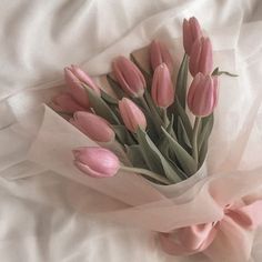 a bouquet of pink tulips is wrapped in white tissue paper on a bed