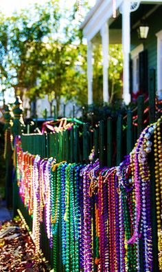 many necklaces are hanging on a green fence in front of a house with trees