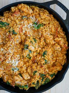 a skillet filled with pasta and spinach covered in parmesan cheese on top of a wooden table