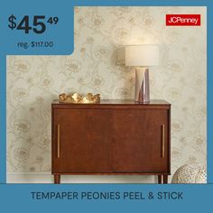 a wooden cabinet sitting next to a lamp on top of a table in front of a wallpapered wall