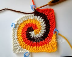 a crocheted square with an orange, white and brown design on the front