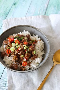 a bowl filled with rice and meat on top of a table next to a spoon