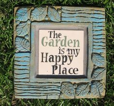 a sign that says the garden is my happy place on green grass with leaves around it